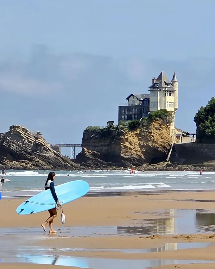 Surfeurs marchant sur la plage avec la Villa Belza en arrière-plan